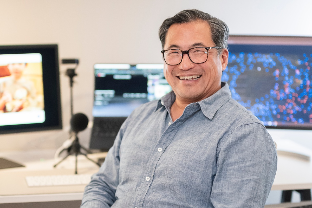 Luyen Chou smiling in front of computer displays in a learning technology workspace