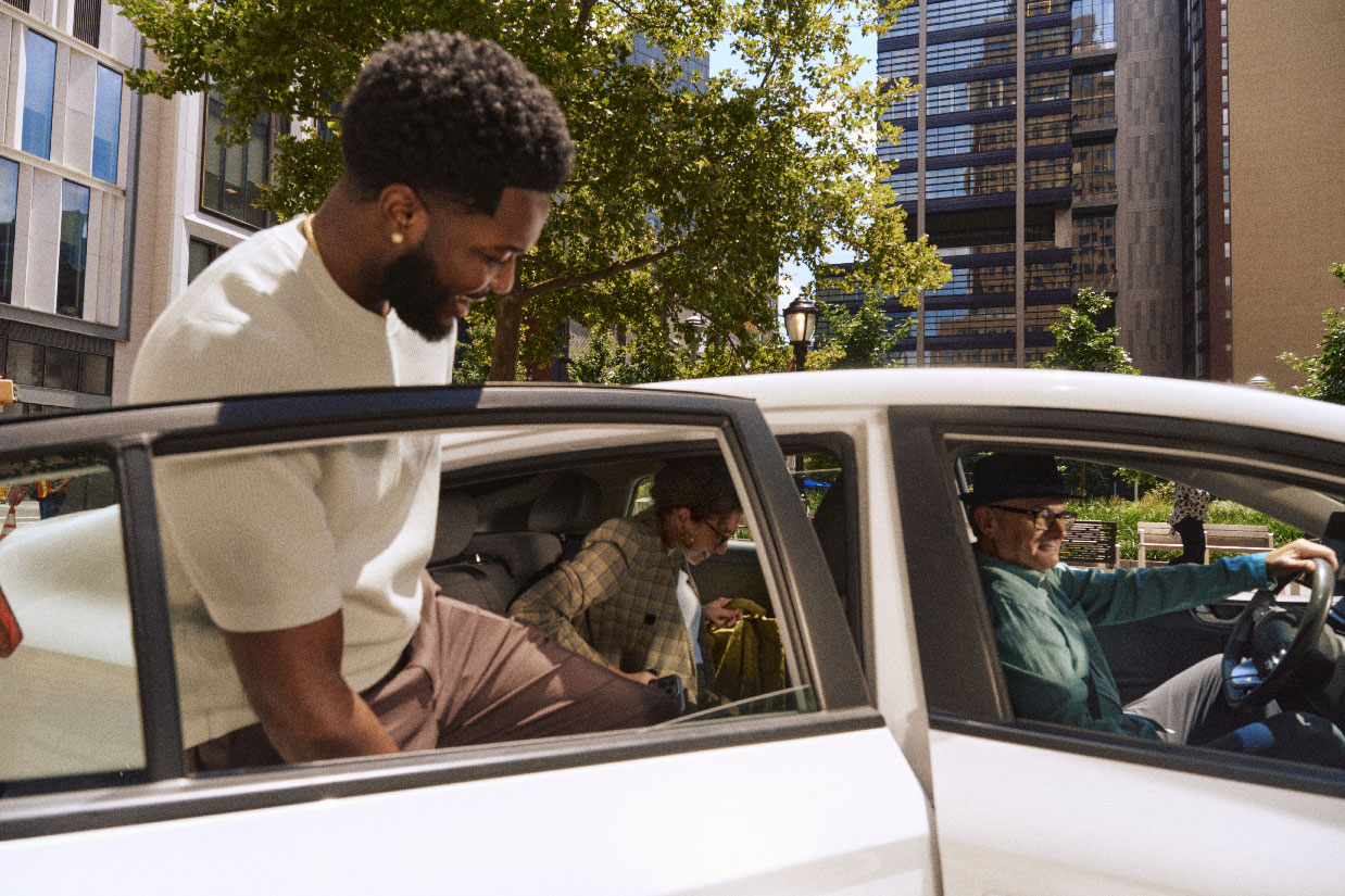 Passengers getting into the back seat of a car while a driver waits