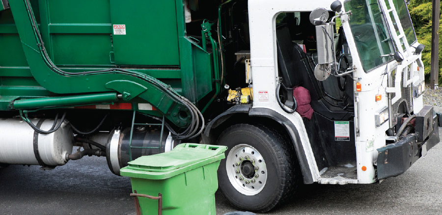 Waste collection truck beside a green bin
