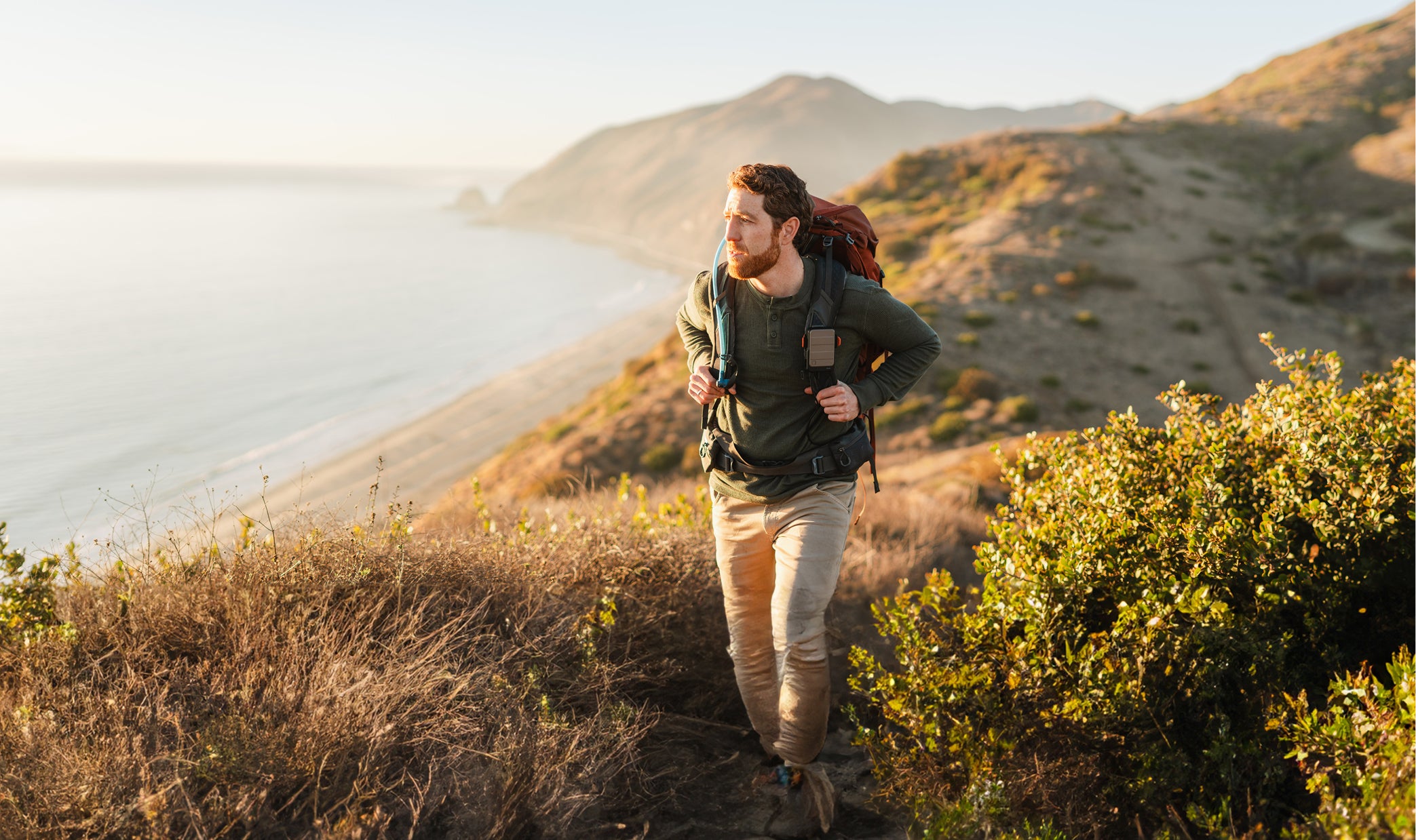 A hiker carrying a pack and a mounted MAAK battery on a coastal trail