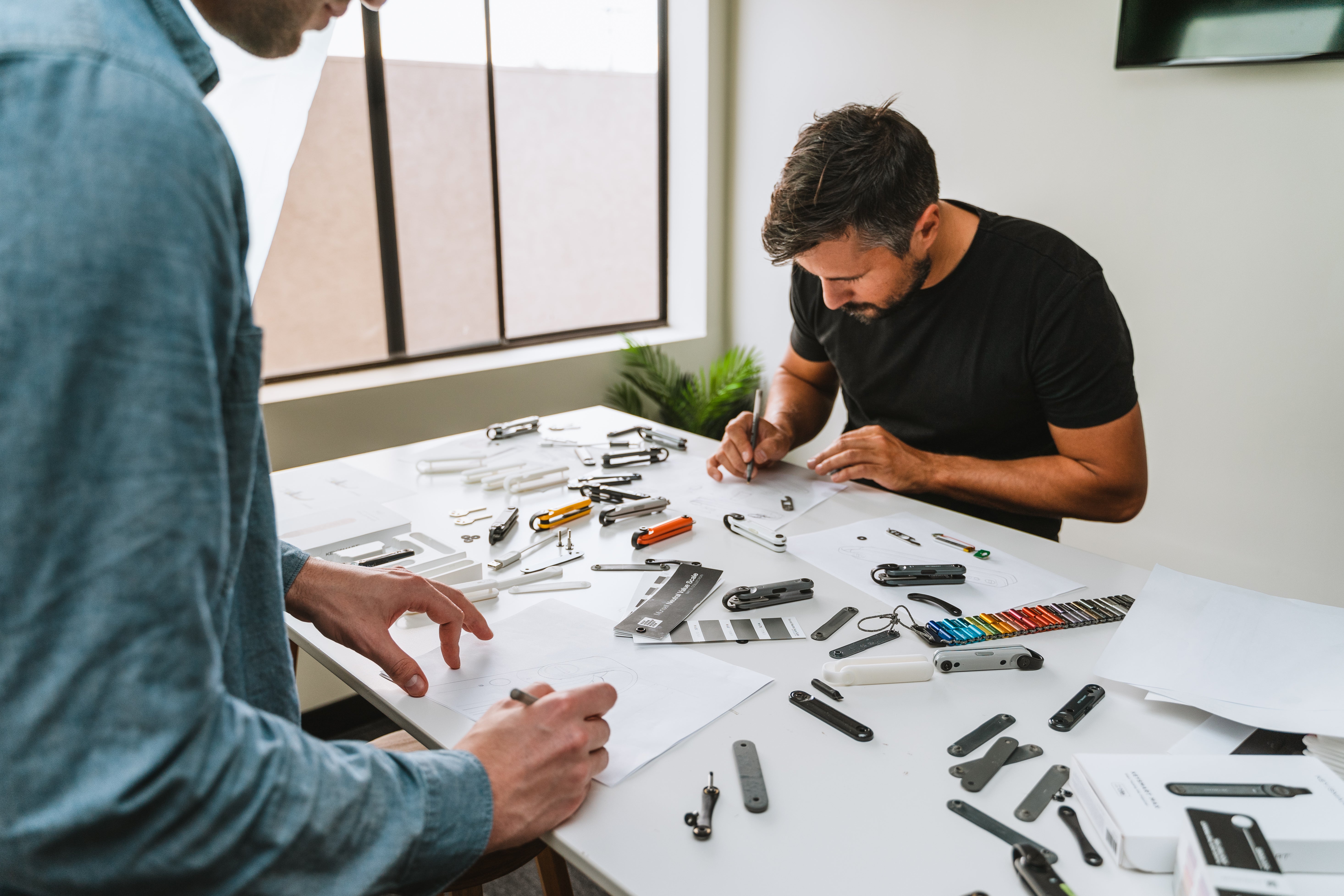 Industrial designers sketching and evaluating hardware prototypes at a white worktable