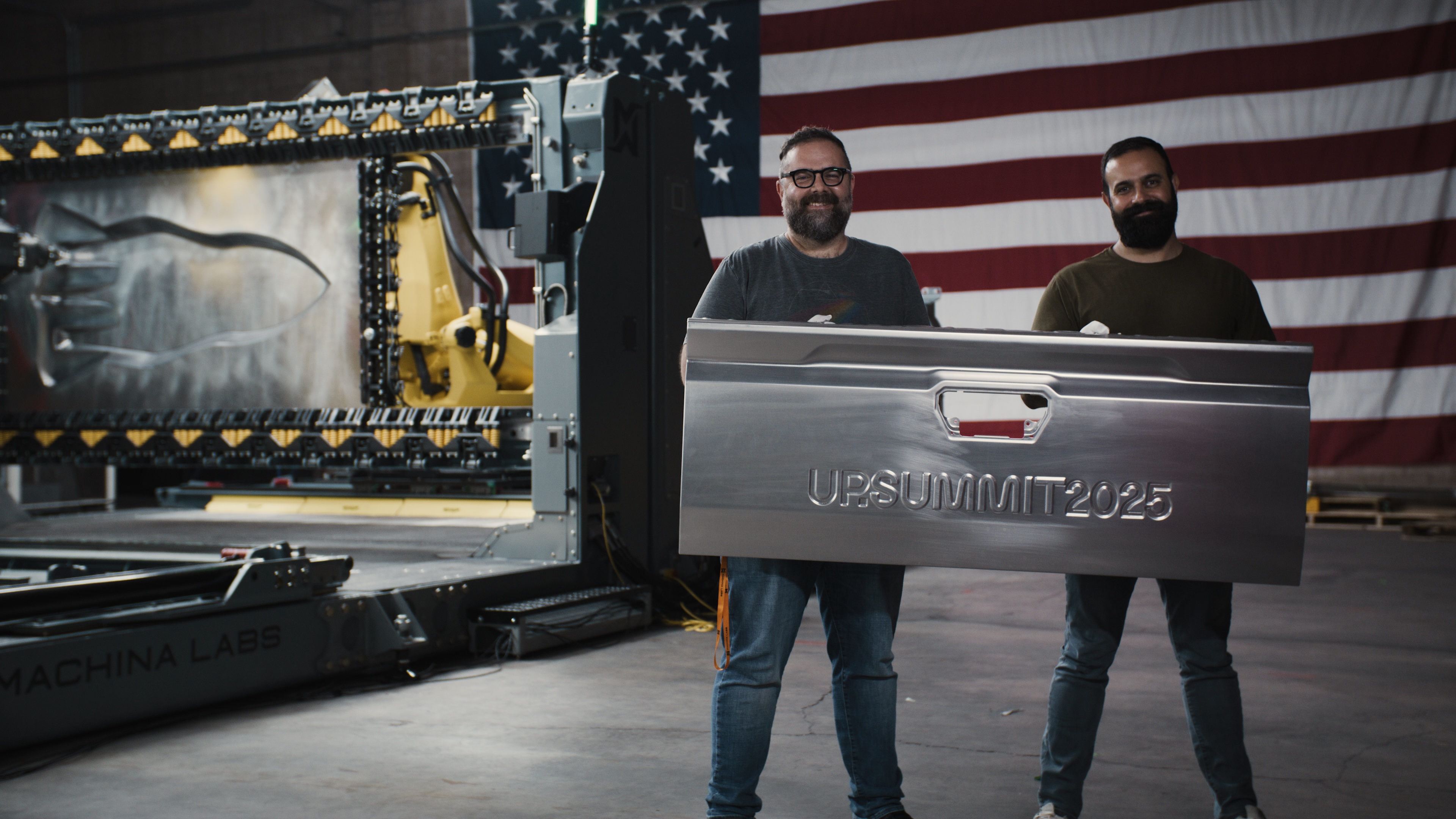 Machina Labs co-founders holding a customized Toyota Tacoma tailgate beside robotic forming equipment