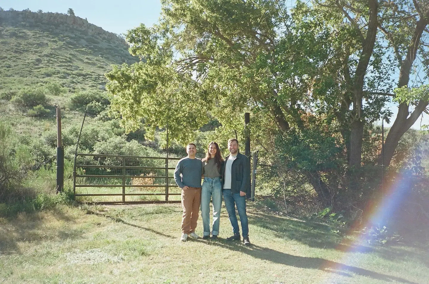 Ambrook cofounders Jeff Anders, Mackenzie Burnett and Dan Schlosser standing together outdoors near a gate and trees