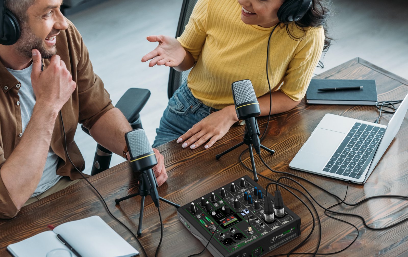 Two people recording a podcast with microphones and headphones on a Mackie mixer