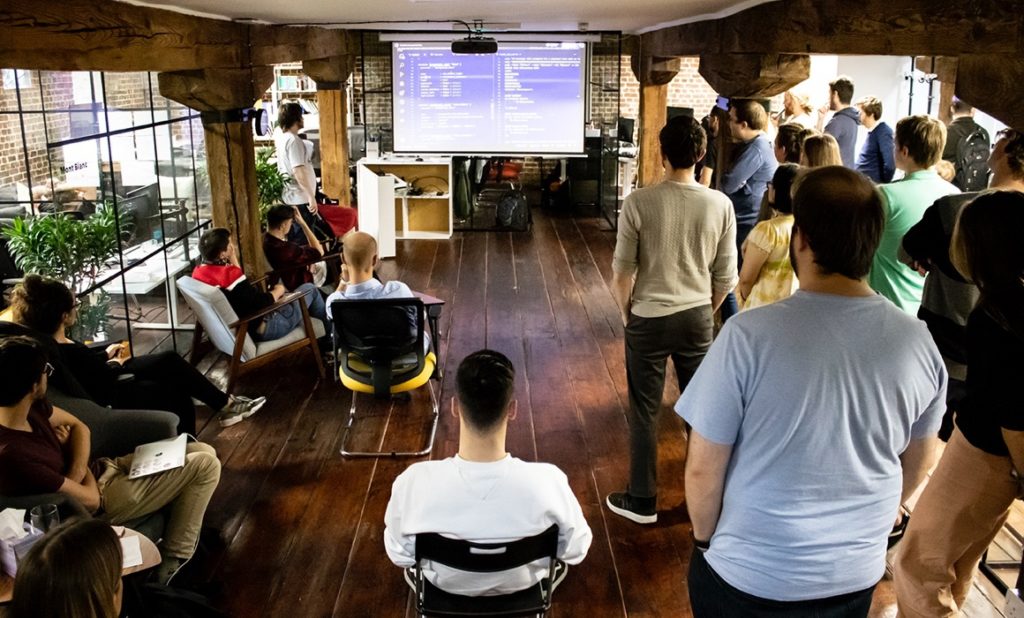 Made Tech colleagues seated and standing around a projected code presentation in a timber-beamed office