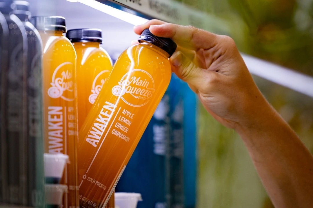 A hand collecting an Awaken juice bottle from a refrigerated Main Squeeze shelf