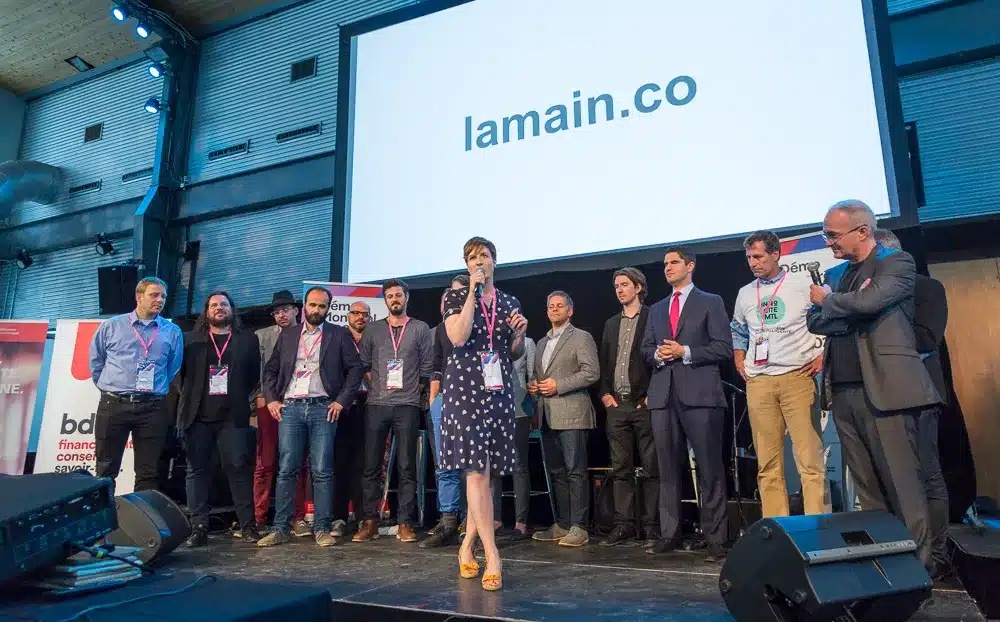 Participants gathered onstage at a MAIN community event, with a speaker holding a microphone