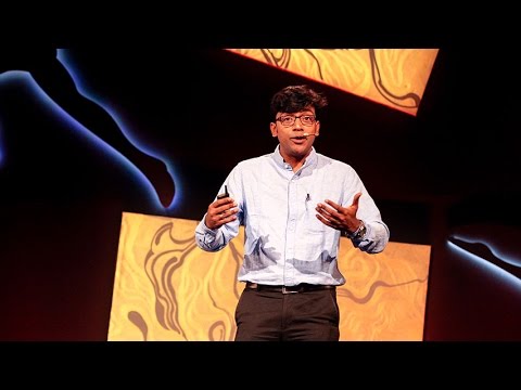 Mainak Chakraborty speaking on stage at INK, wearing a light shirt and holding a presentation remote