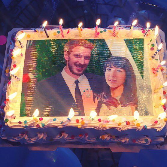 Birthday cake with a digitally edited photograph of Miley Cyrus and a man, surrounded by lit candles