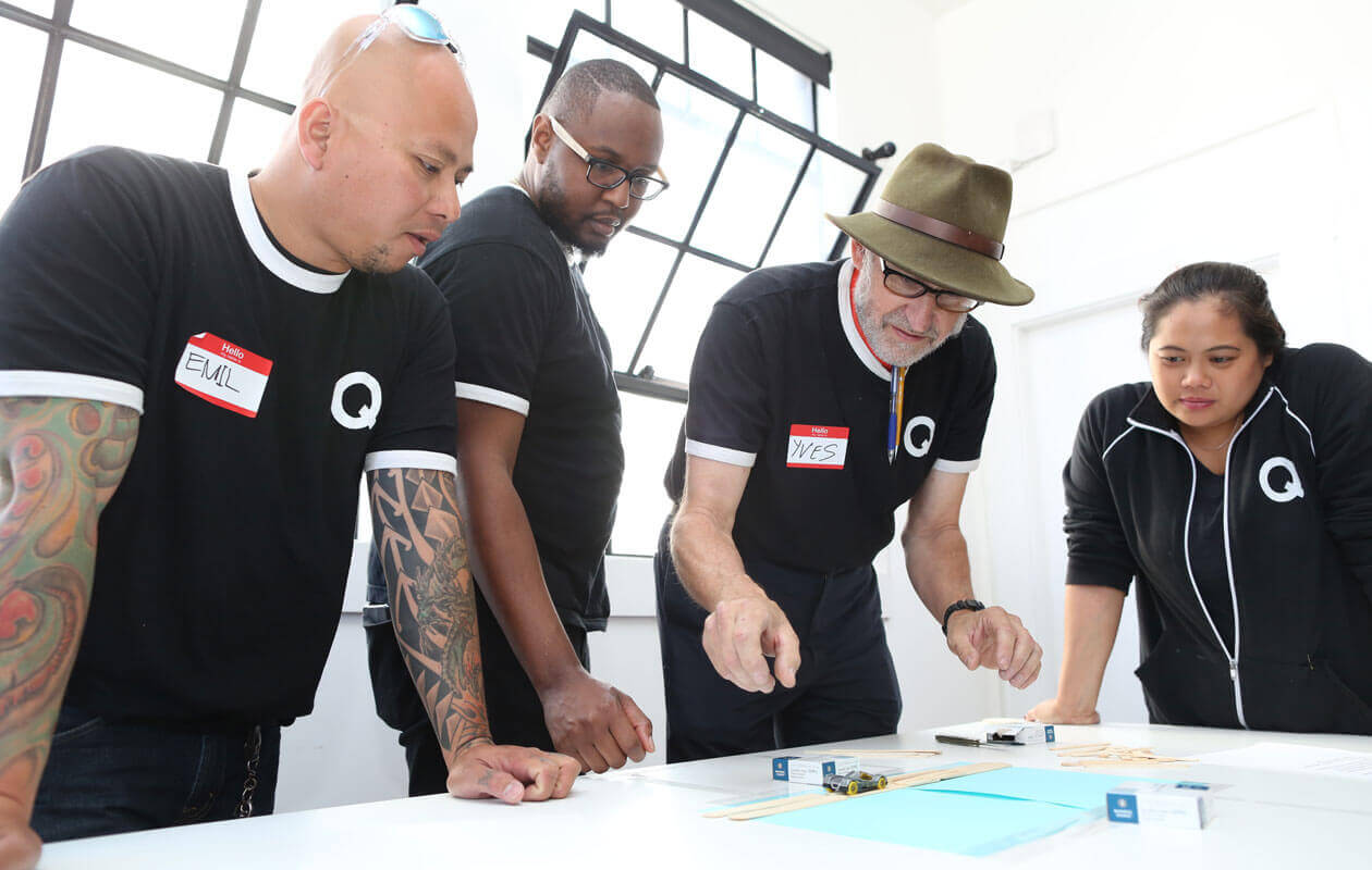 Four Q Services team members in Q shirts gathered around a table