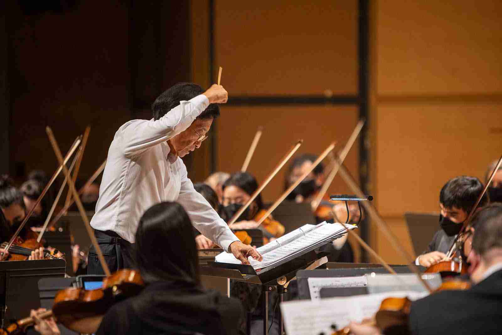 Mandle Cheung following the score while conducting the Mandle Philharmonic, with string players around him