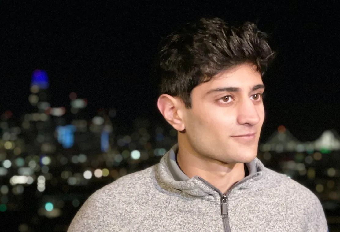 Maneet Khaira wearing a grey quarter-zip with city lights behind him