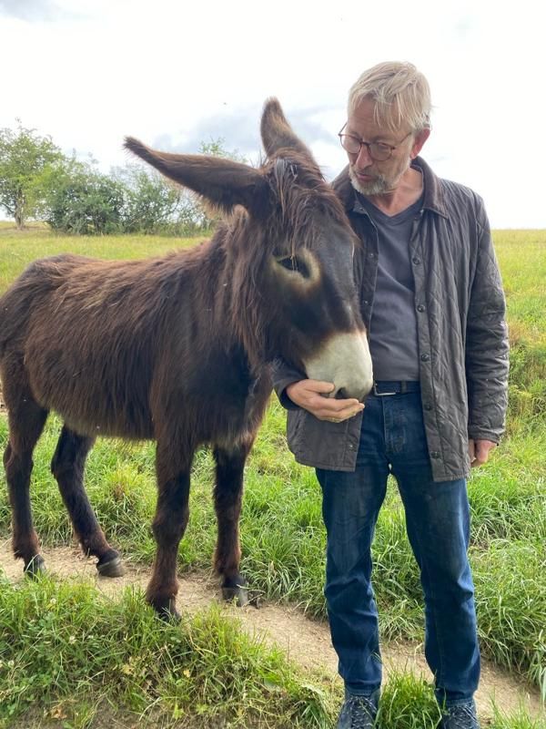Manfred Ruediger standing outdoors beside a donkey, with his hand beneath its muzzle