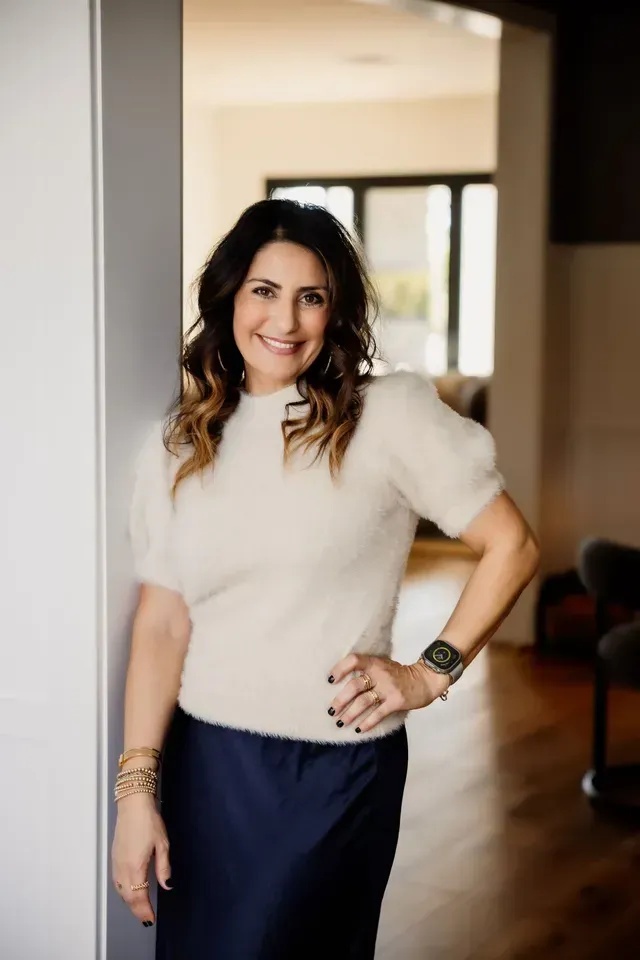 Mania Persekian standing in a doorway, in a white top and dark trousers