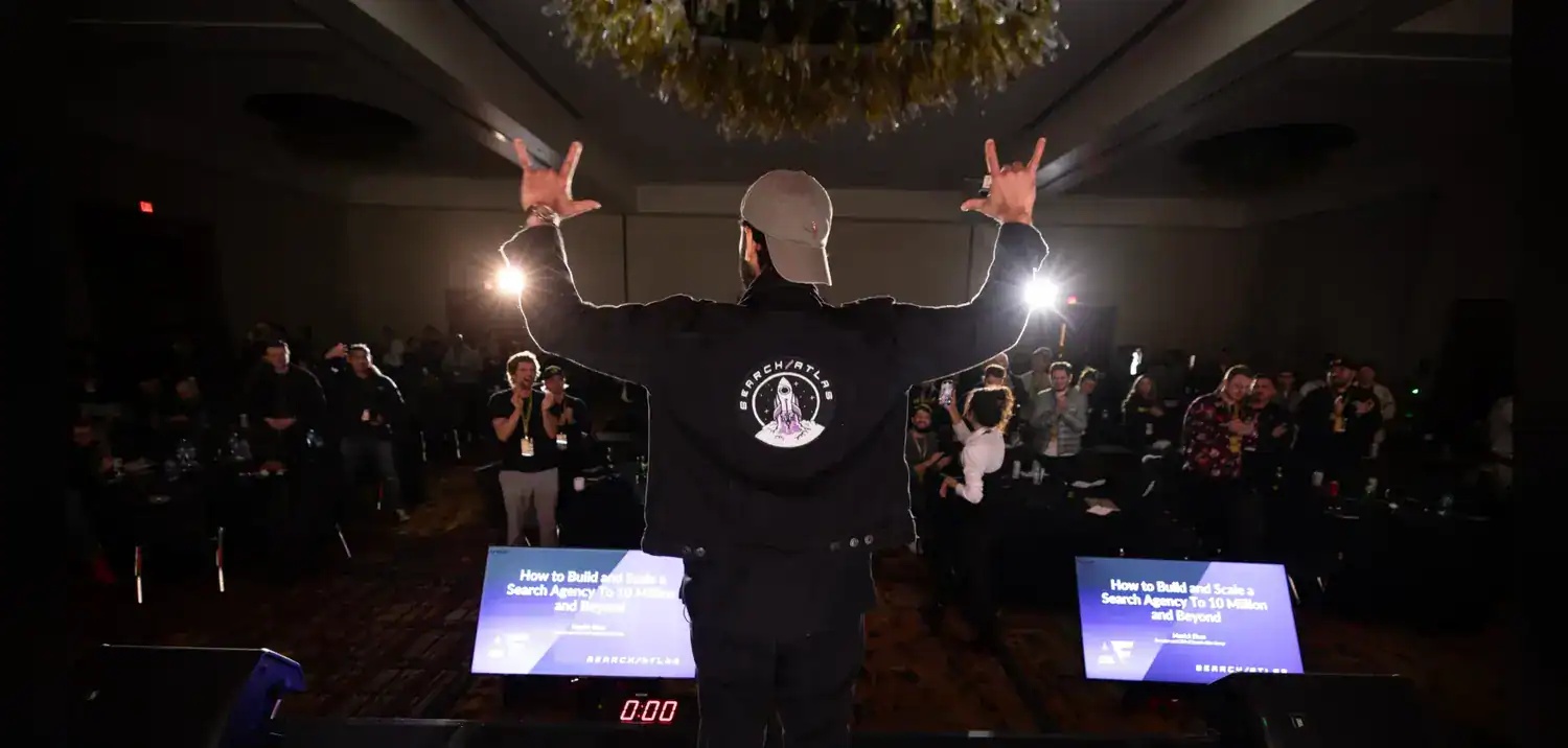 Manick Bhan facing an applauding conference audience with both arms raised