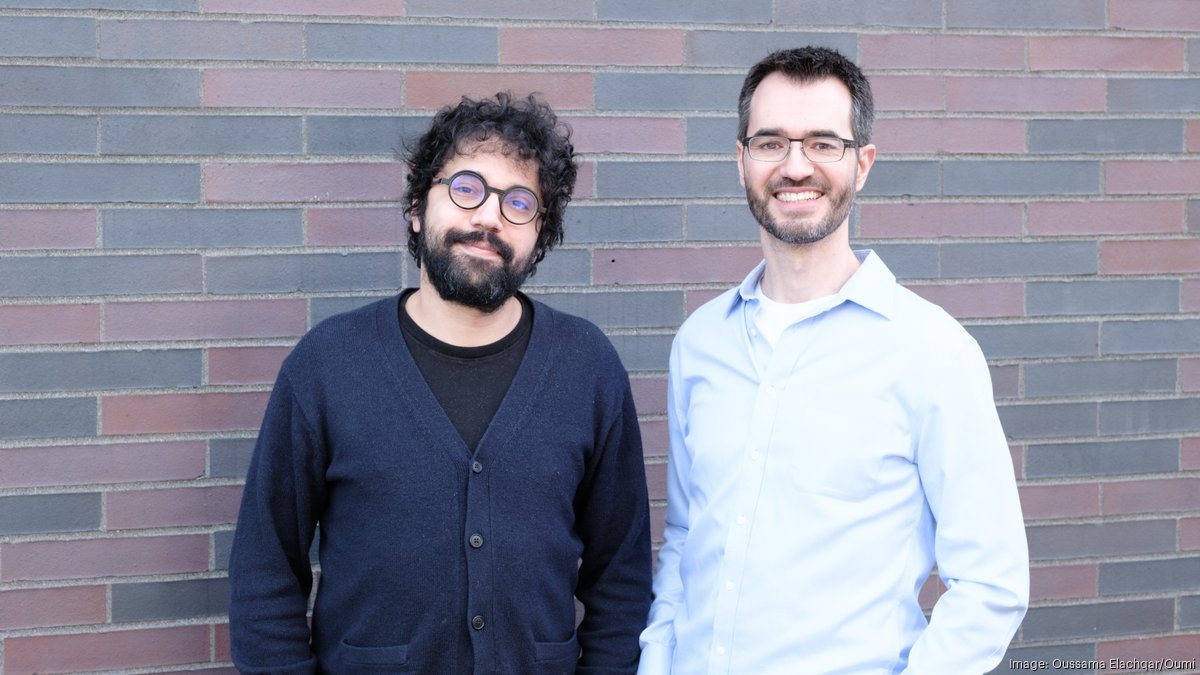 Oumi co-founders Oussama Elachqar, left, and Manos Koukoumidis, right, standing beside a brick wall