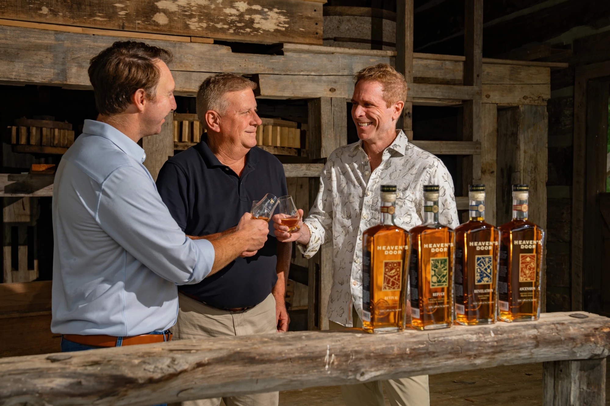 Marc Bushala, at right, smiling with two Heaven’s Door colleagues beside a display of whiskey bottles.