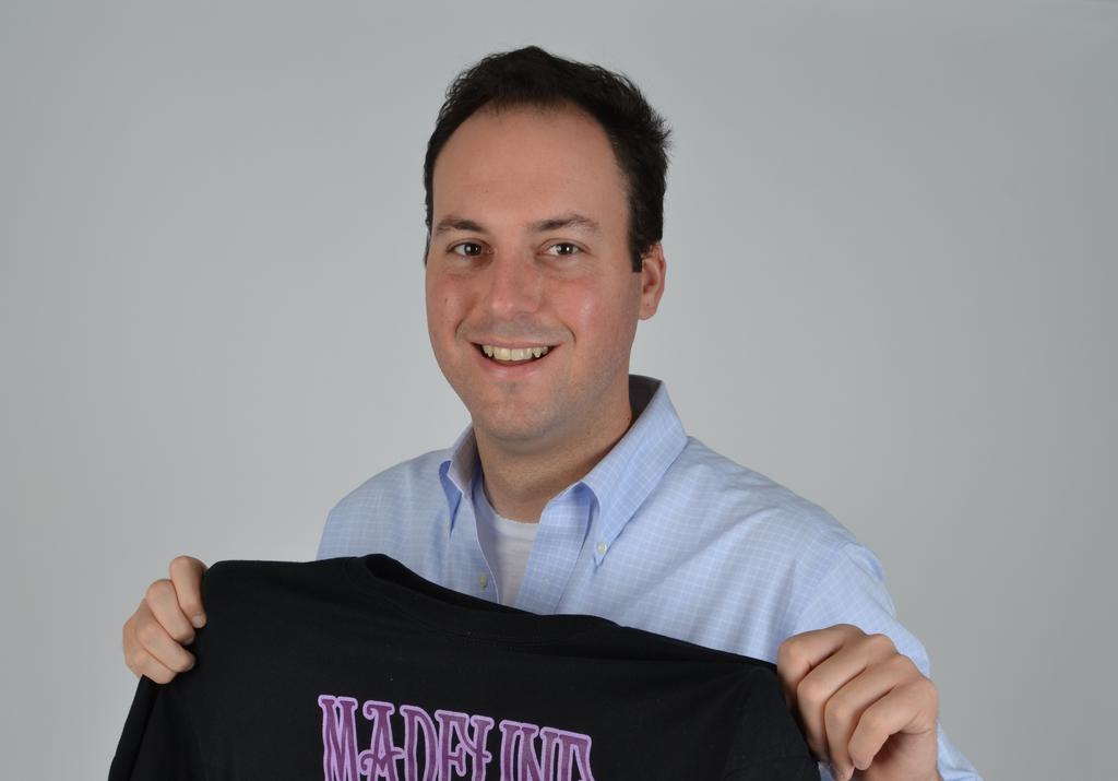 Marc Katz smiling while holding a black T-shirt in a press photograph
