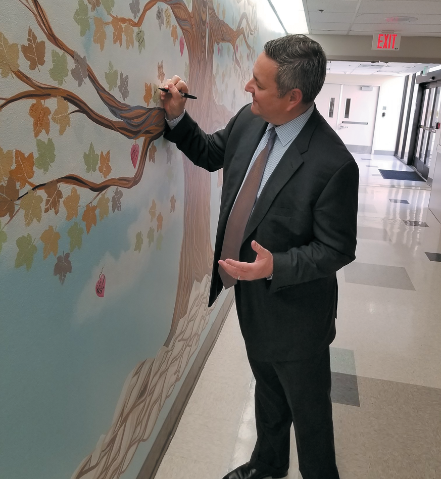 Marc Miller reaches up to sign a leaf on the employee Vision Tree display.