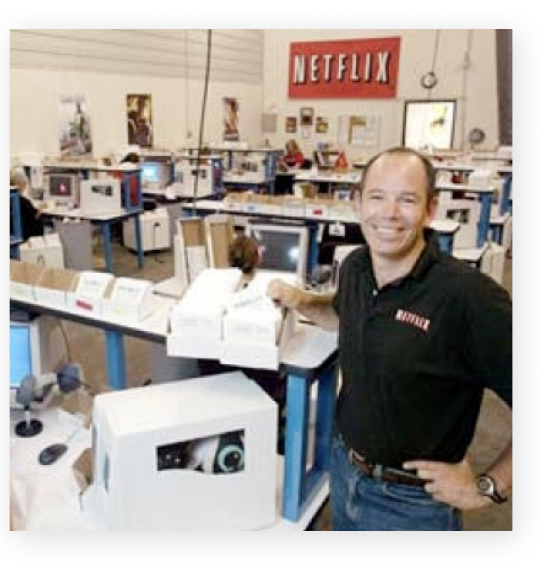 Marc Randolph standing among desks and computer monitors at the Netflix office in 1999