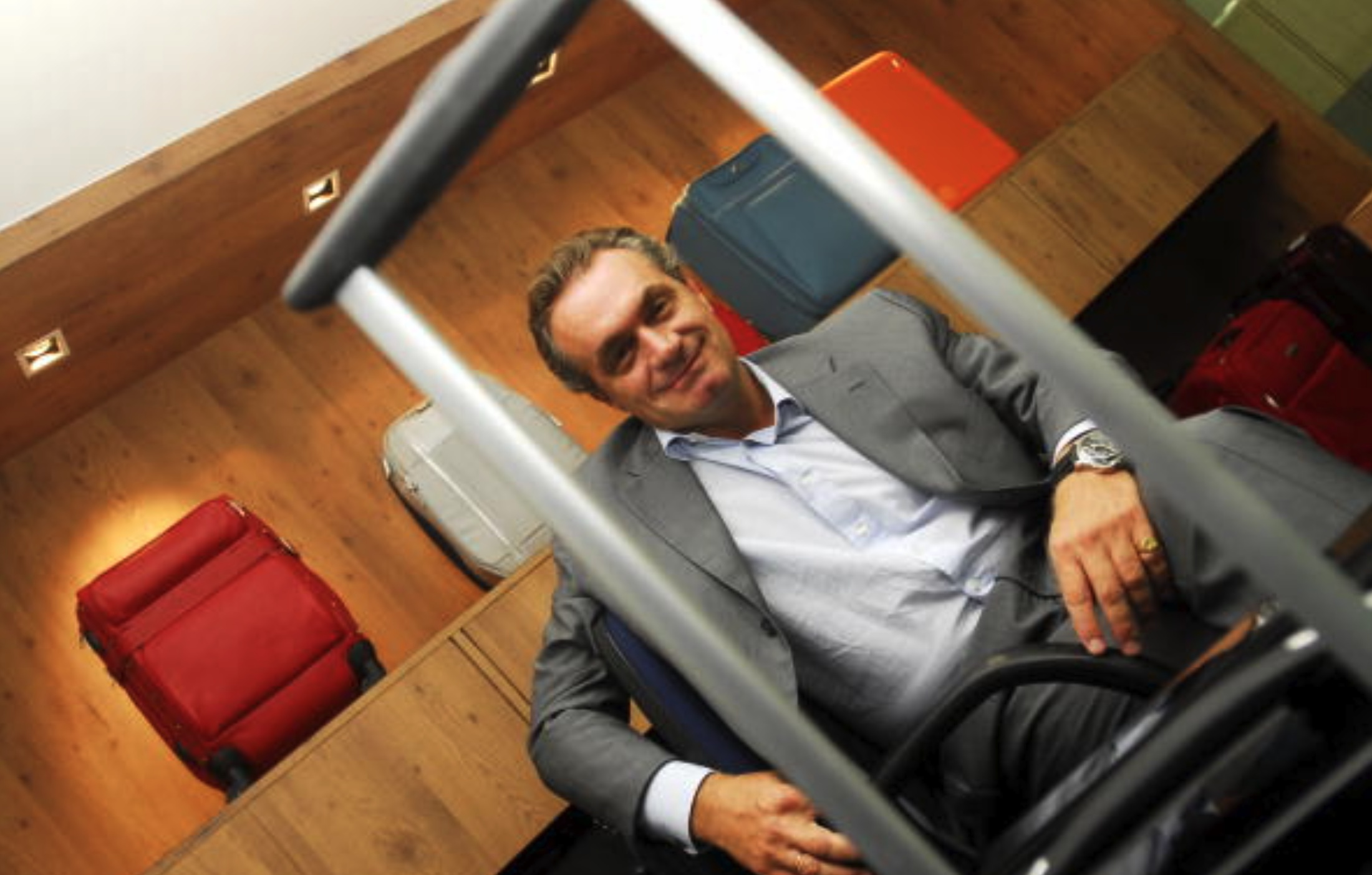 Marcello Bottoli seated in a luggage showroom, framed by suitcase handles and colorful cases on wooden shelves