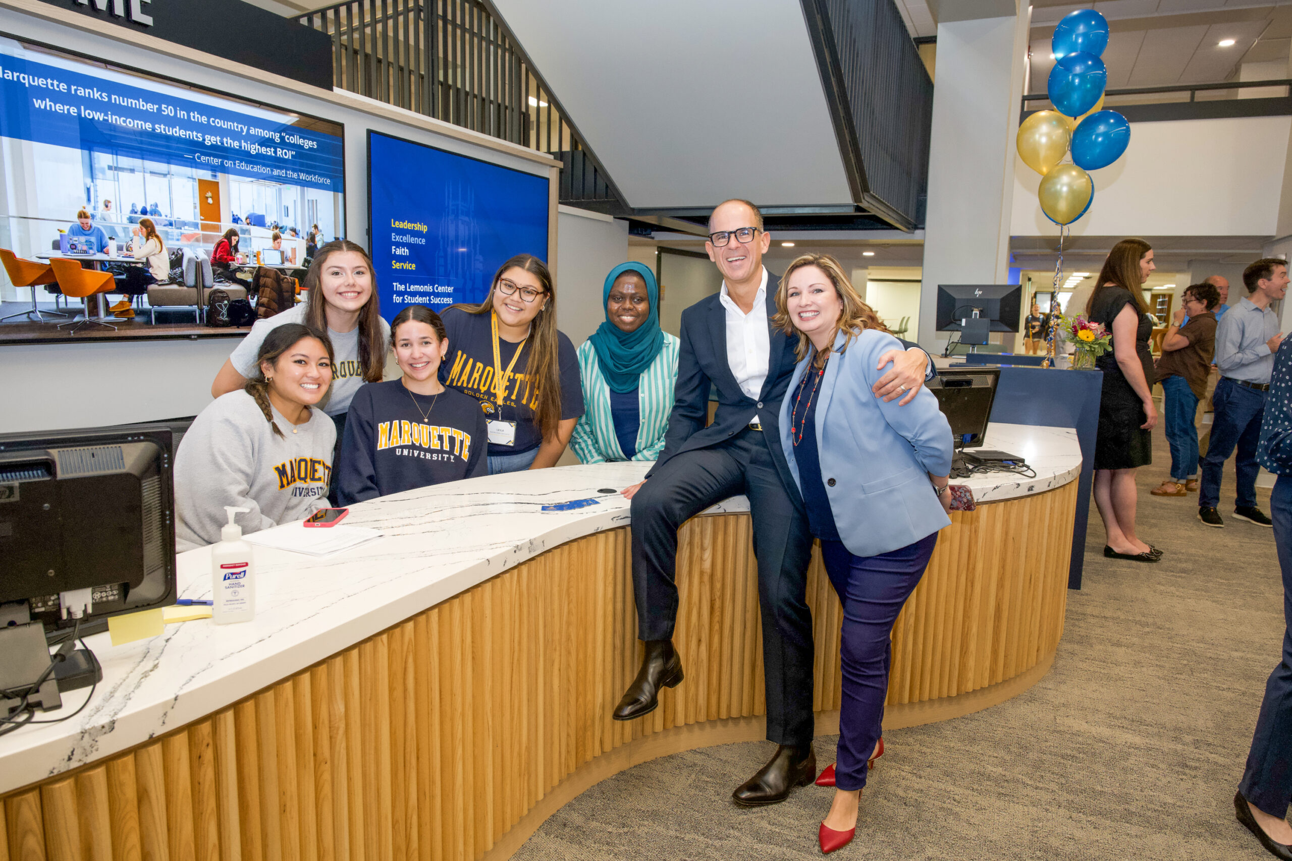 Marcus Lemonis sits on the Ask Me Desk with students and center director Marilyn Jones at Marquette