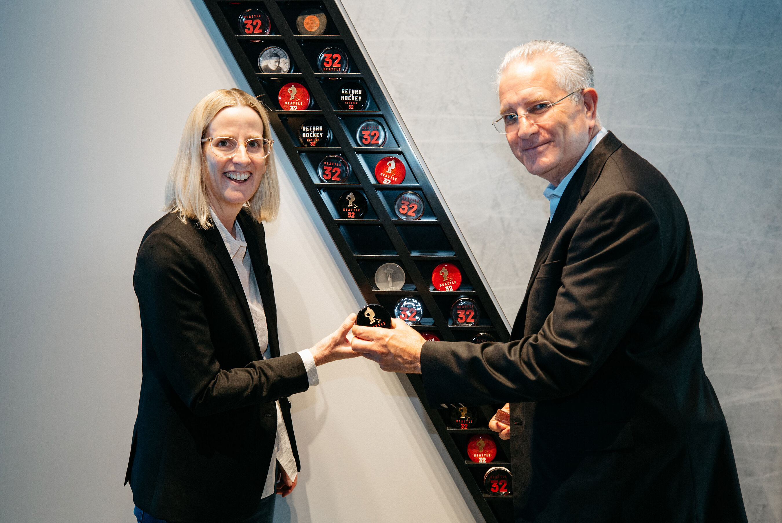 Margaret Meister and Tod Leiweke hold a hockey puck at the NHL Seattle Preview Center.