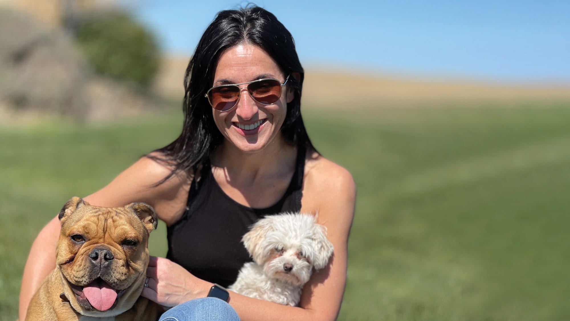 Margi Tooth sitting outdoors with an English Bulldog and a small white Maltipoo