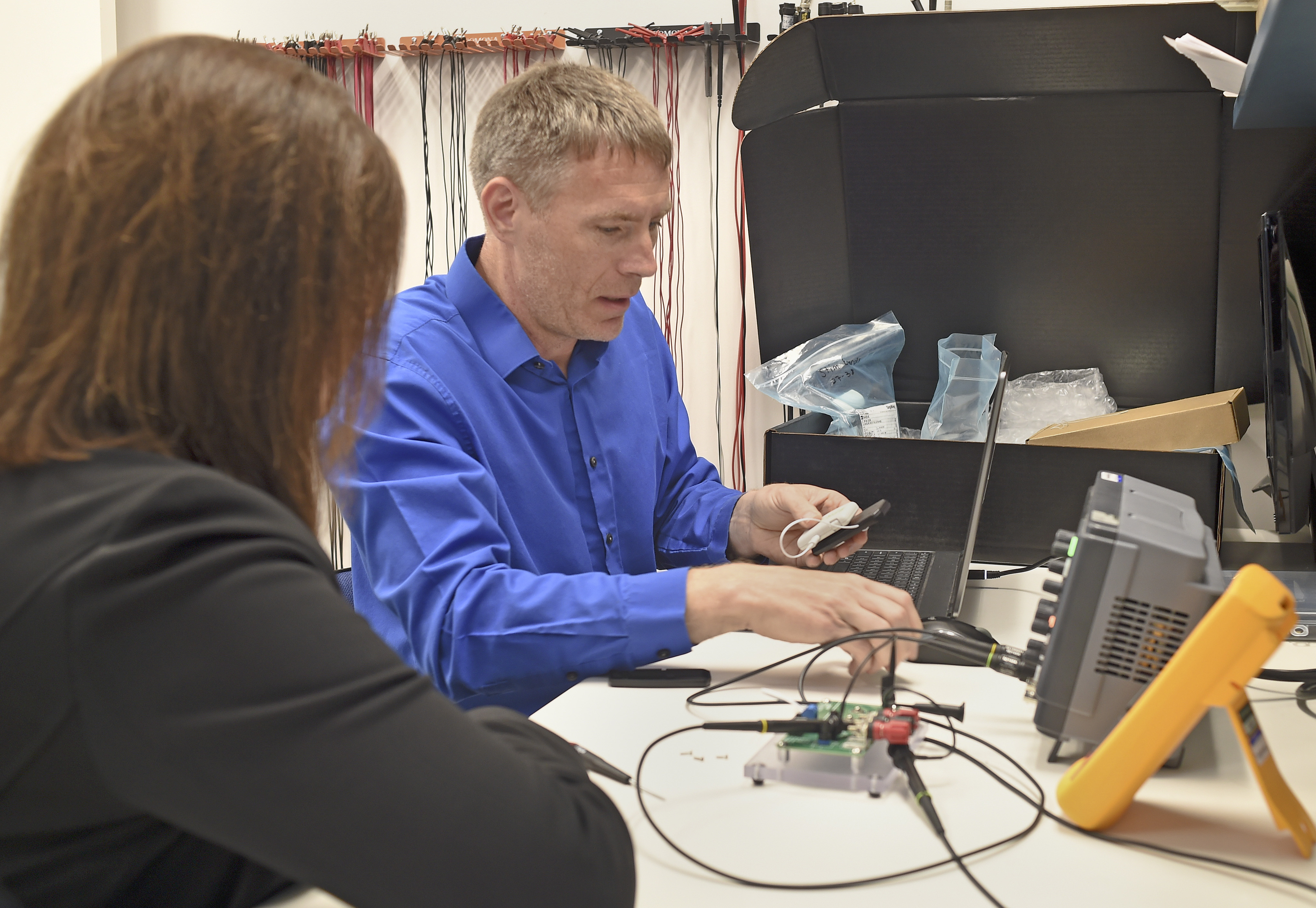 Maria Bennett observes an SPR engineer testing electronics at a laboratory workbench
