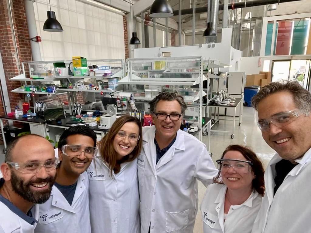 Six members of the Triplebar team wearing laboratory coats and safety glasses in a laboratory