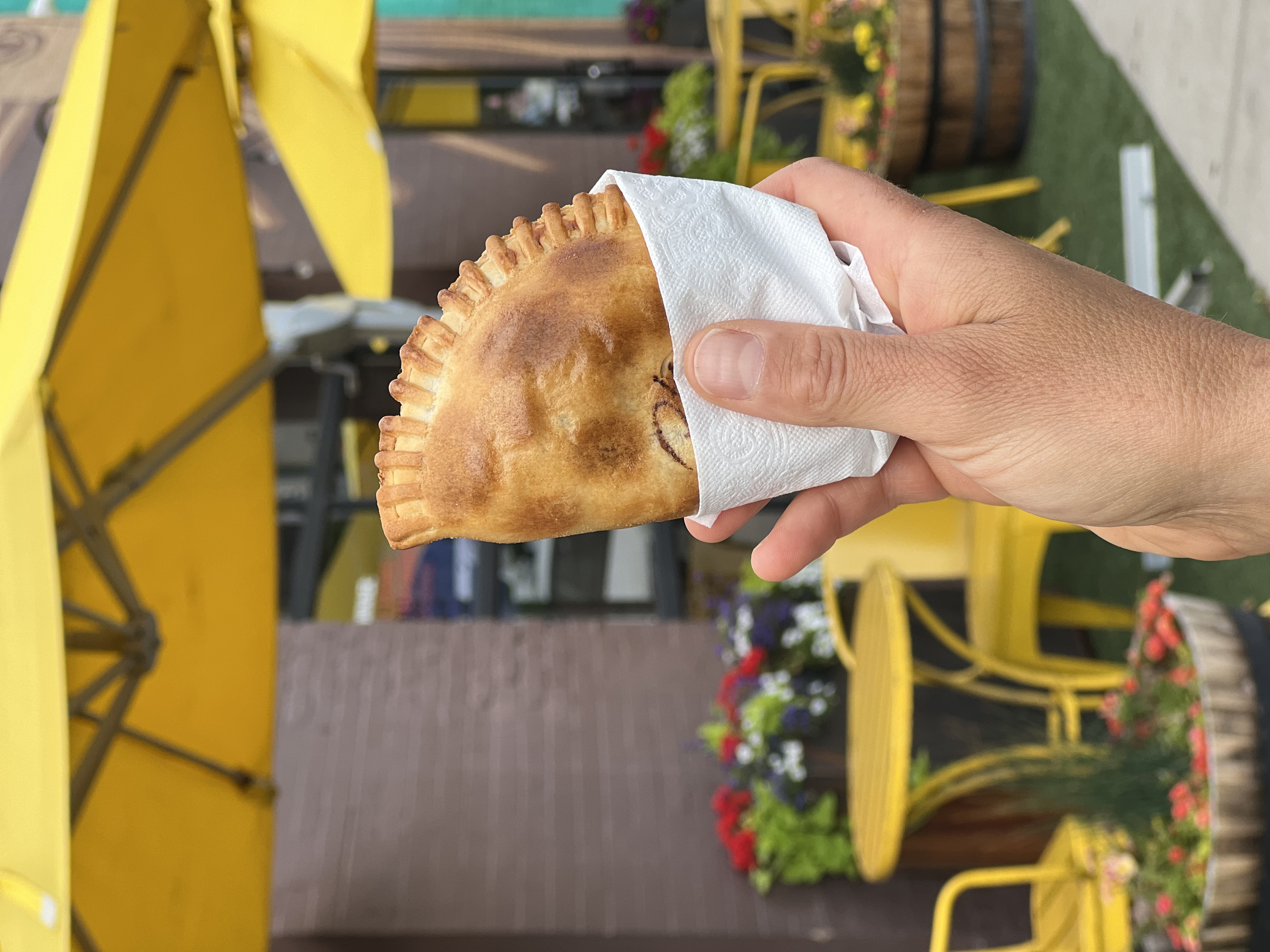 A hand holding a single baked Maria Empanada on the patio