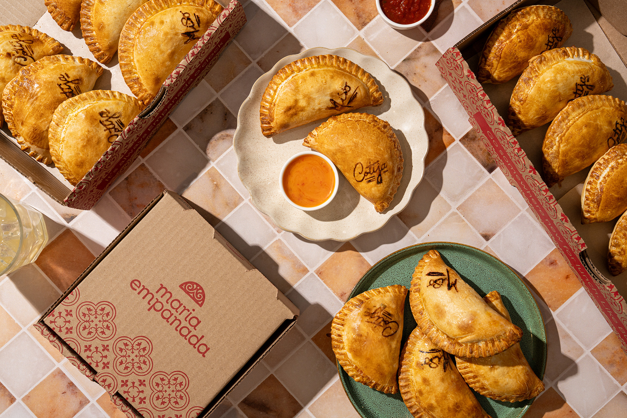 An array of Maria Empanada empanadas with branded takeout boxes and dipping sauces