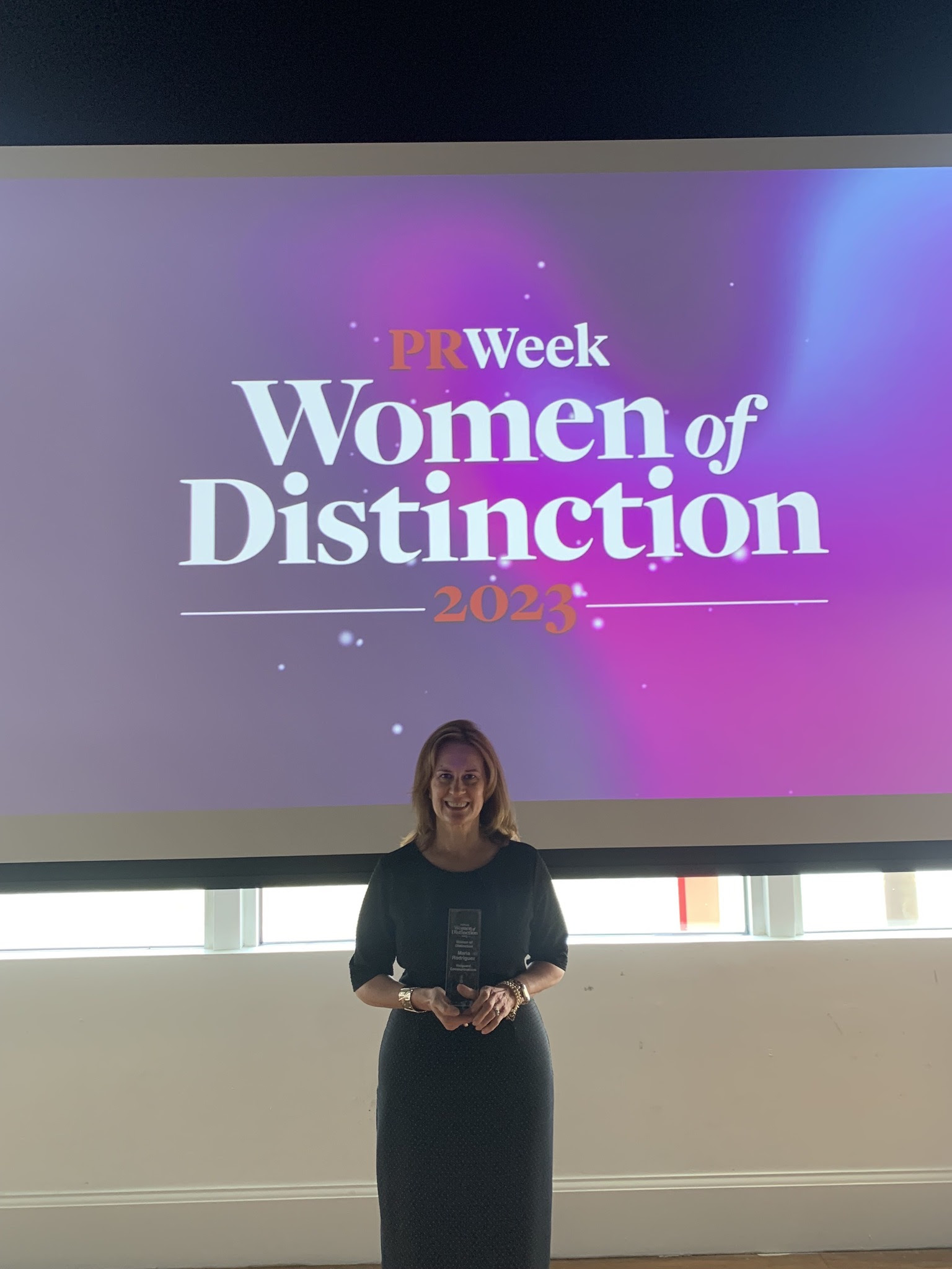 Maria Rodriguez holding her award in front of a PRWeek Women of Distinction 2023 screen