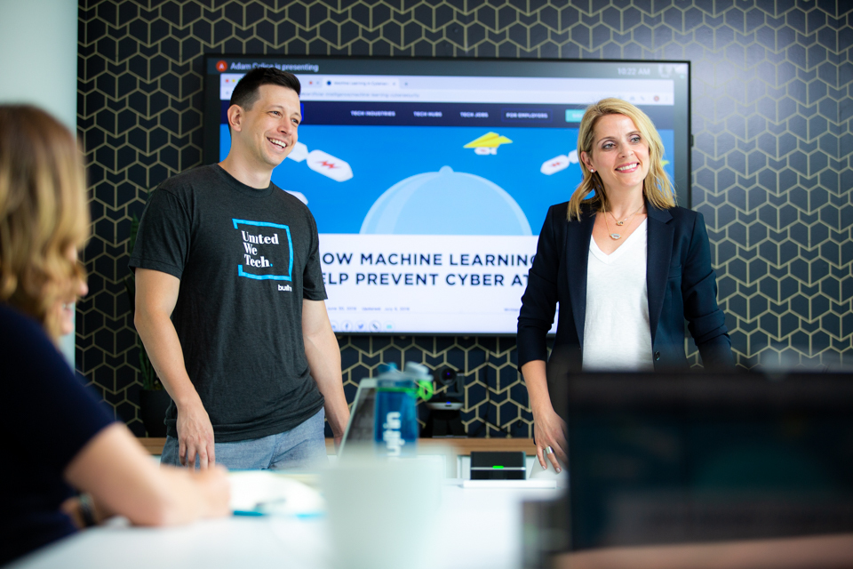 Maria Katris and Adam Calica standing at the front of a Built In team meeting
