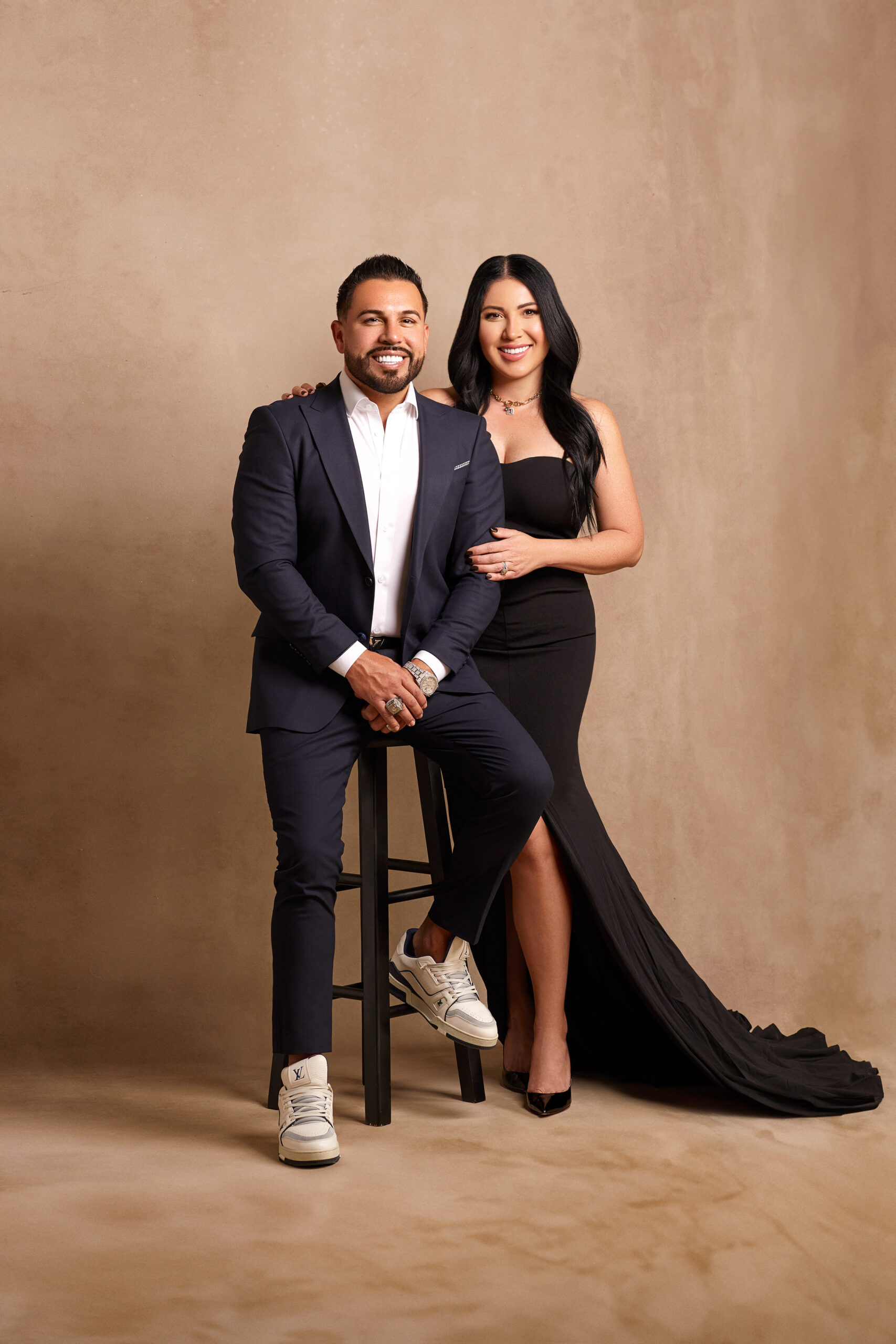 Mario and Franny Arrizon photographed together, Mario seated in a suit and sneakers and Franny standing beside him