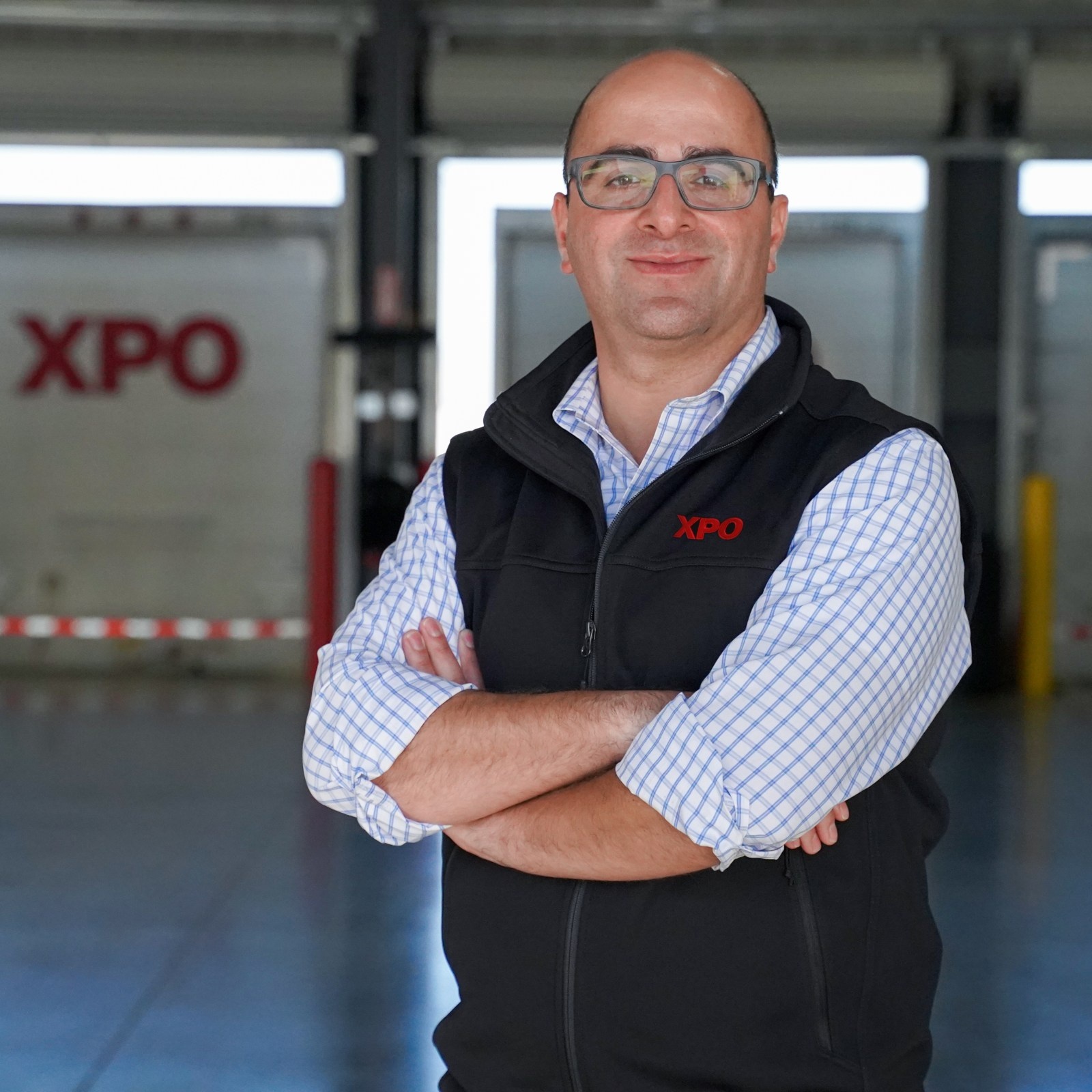 Mario Harik in an XPO vest, standing in front of loading doors at a freight facility