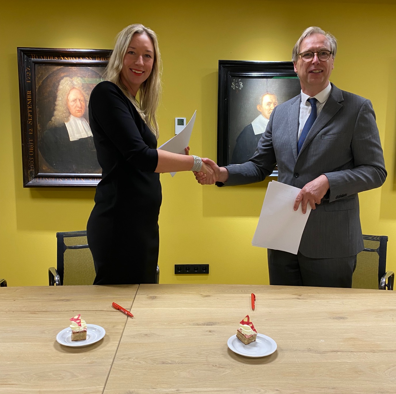 Marjella Lecourt-Alma and Campus Fryslân dean Tjalling Halbertsma shaking hands, holding their partnership documents.