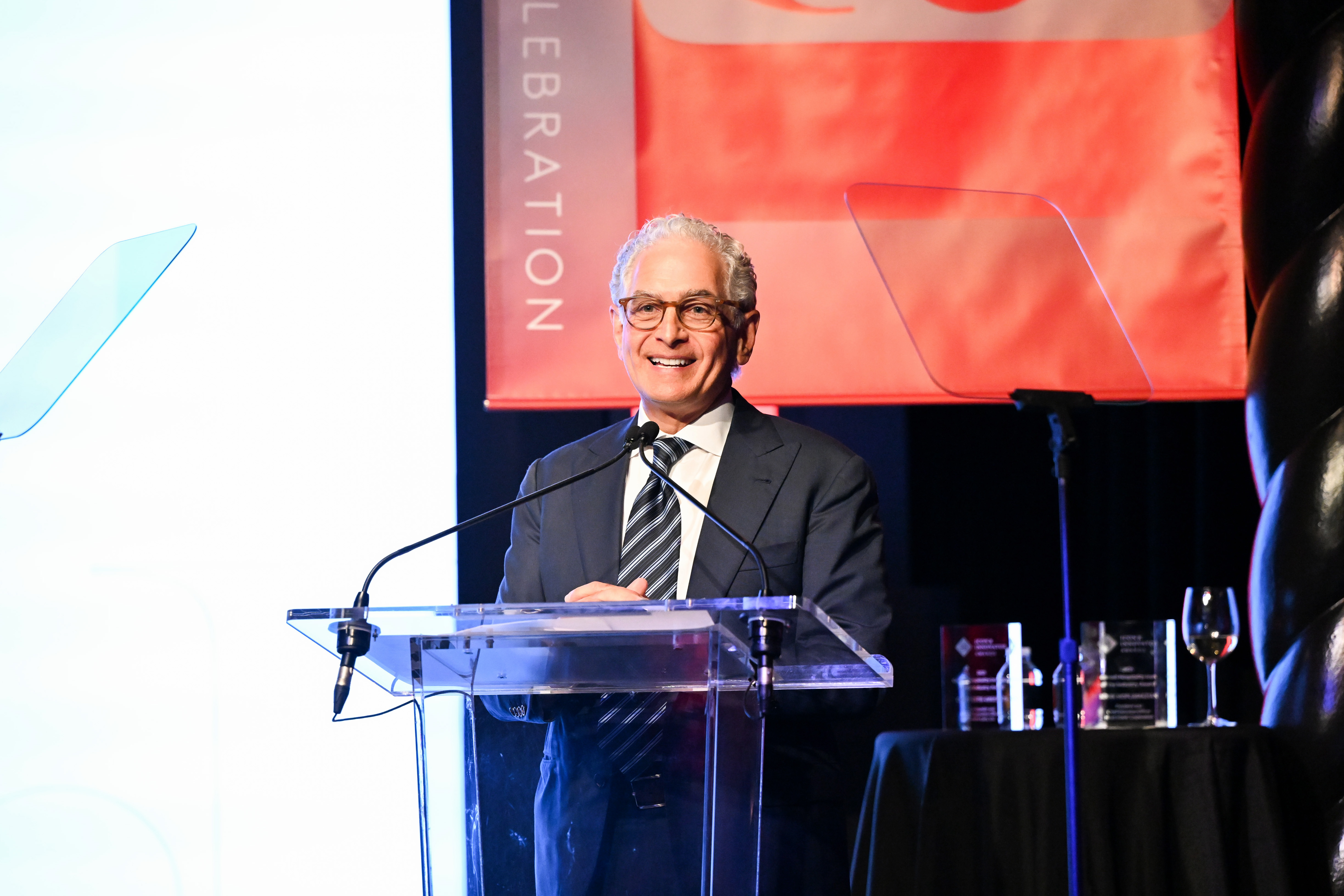 Mark Hoplamazian smiling while speaking at a clear lectern at the 2025 Cornell hospitality awards