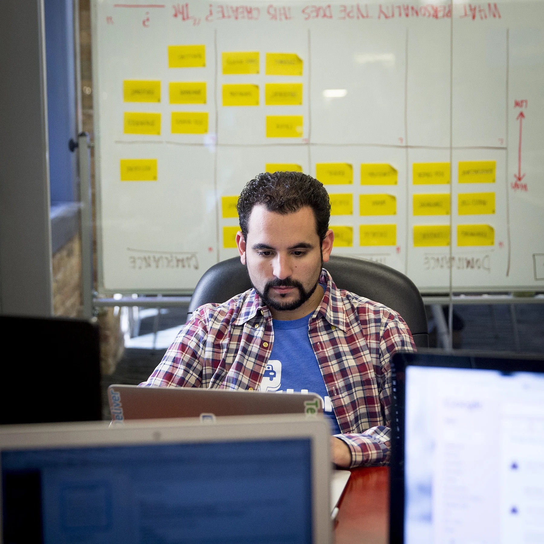 Mark Lawrence working at a laptop, with monitors and a planning board around his desk