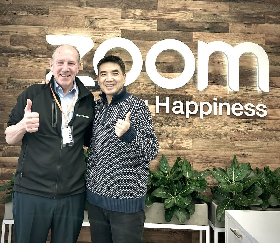 Mark Loehr, left, and Zoom founder Eric Yuan smiling together in front of a Zoom sign.