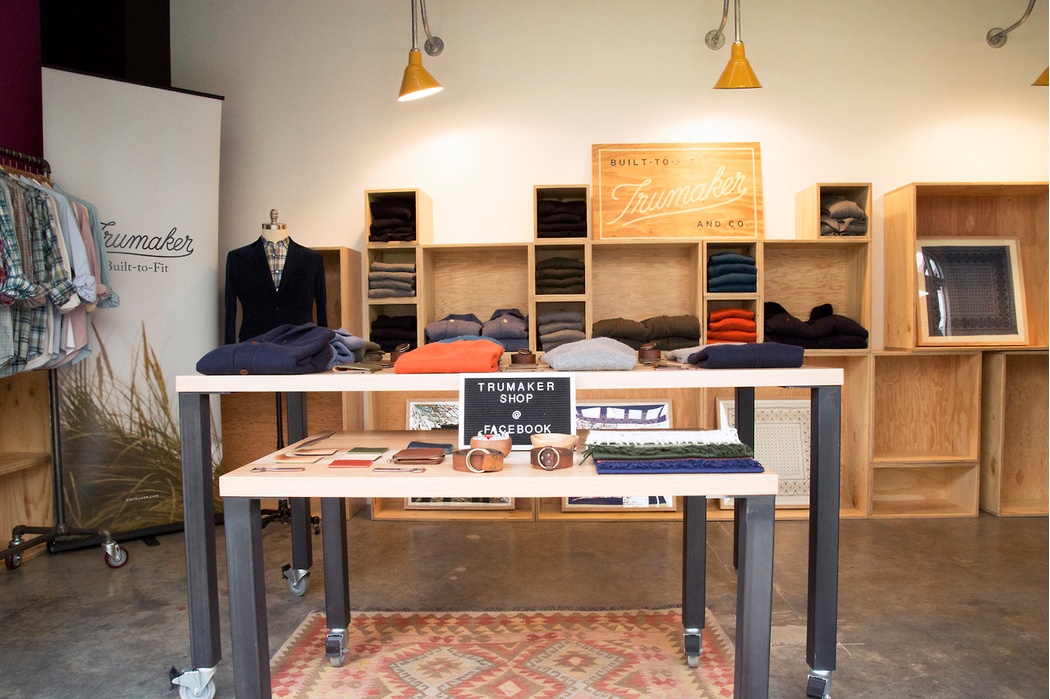 Trumaker clothing display with folded sweaters, shirts, belts and a blazer