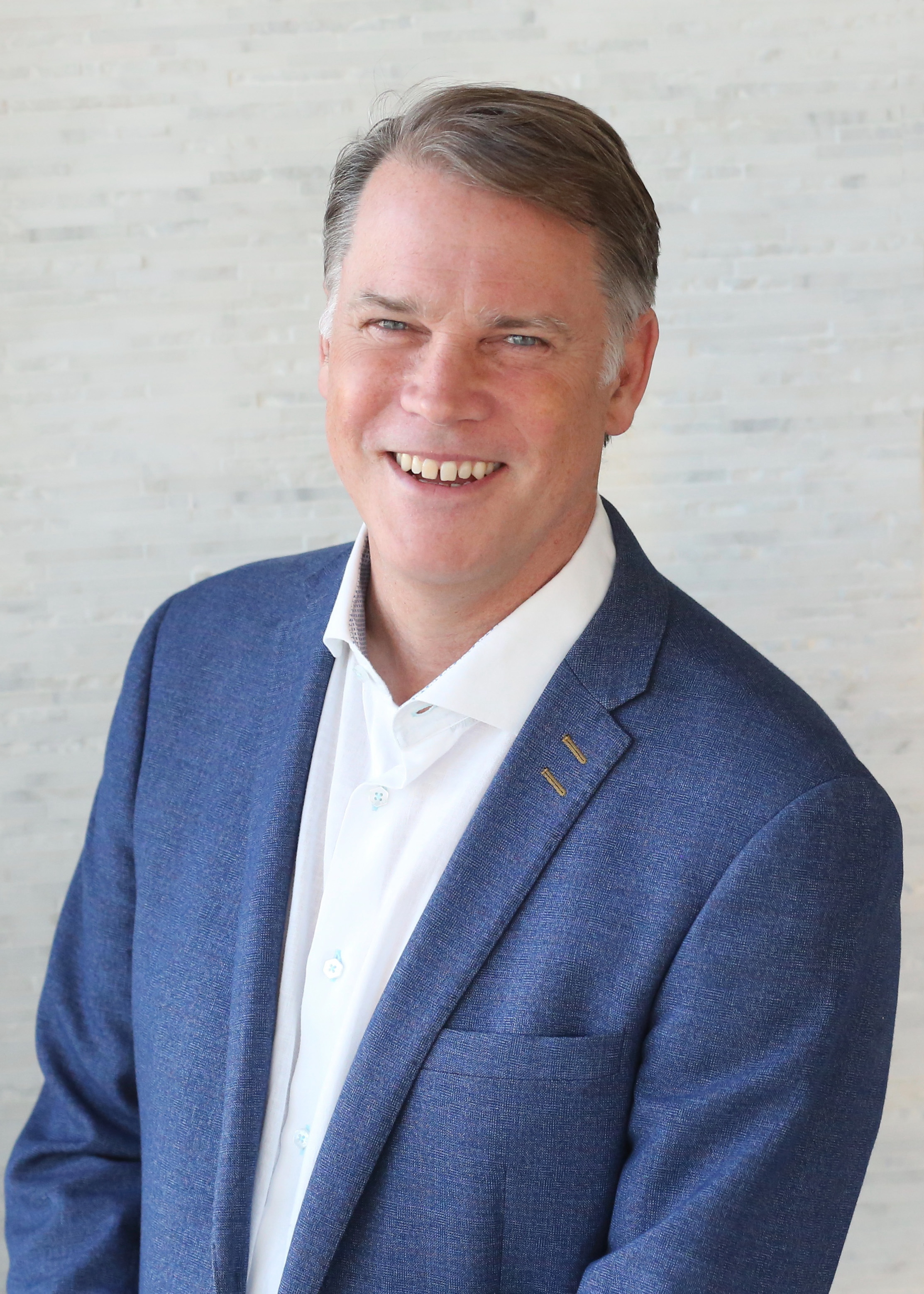 Mark Palmer in a blue jacket against a light textured wall