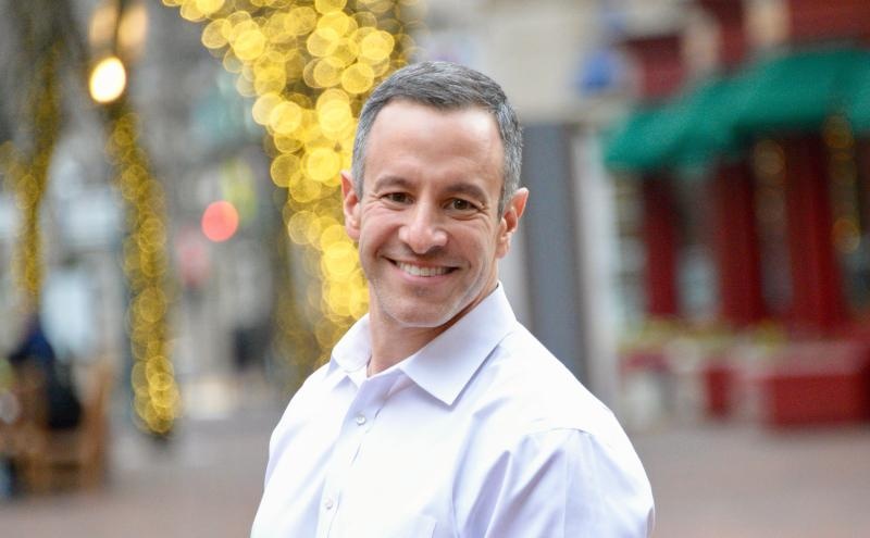 Mark Simons in a white shirt on a pedestrian street, with lights behind him