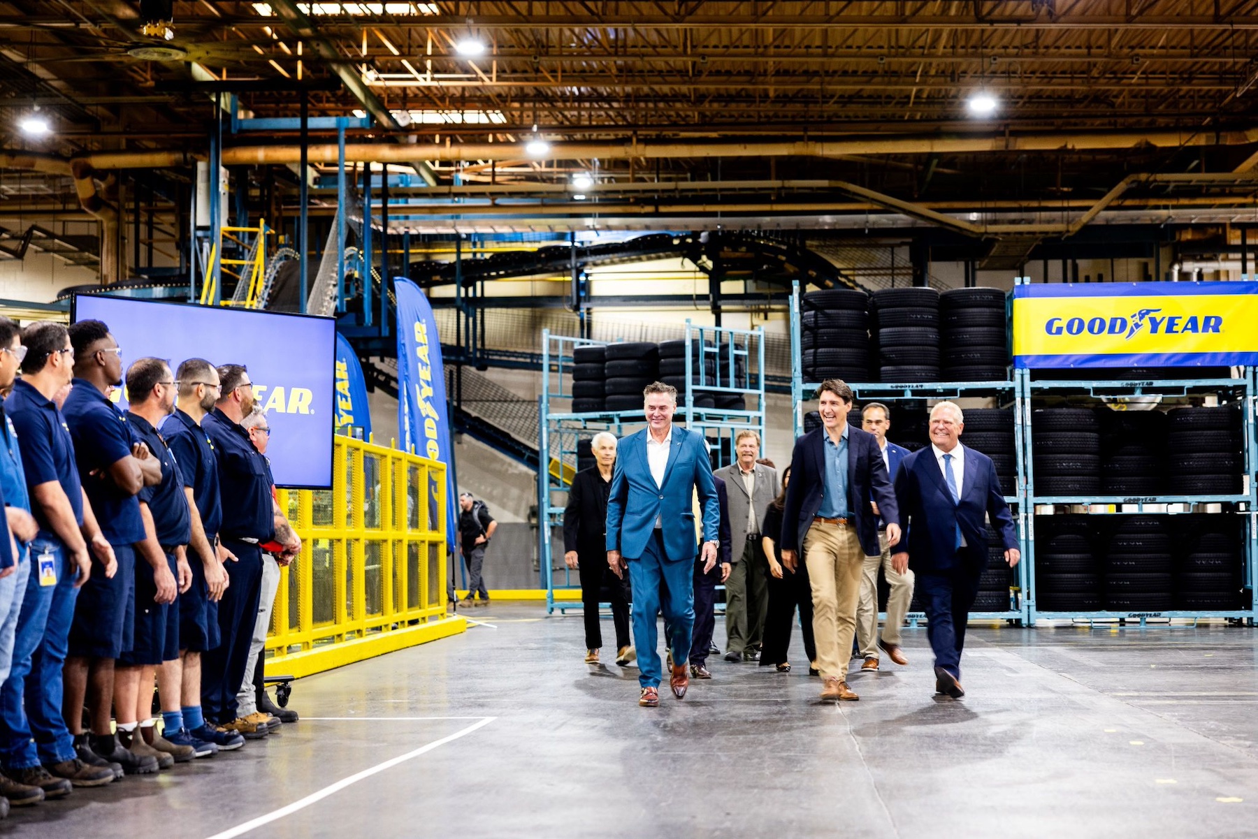 Mark Stewart walks through Goodyear’s Napanee factory with Justin Trudeau and Doug Ford, beside employees and racks of tires.