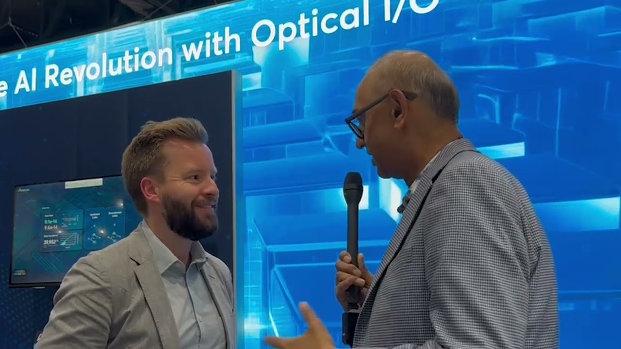 Mark Wade speaking with an interviewer beside an Ayar Labs optical I/O display at OFC 2024