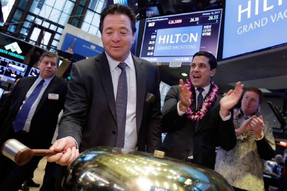 Mark Wang holding a gavel beside a brass bell on the New York Stock Exchange trading floor, with colleagues applauding.