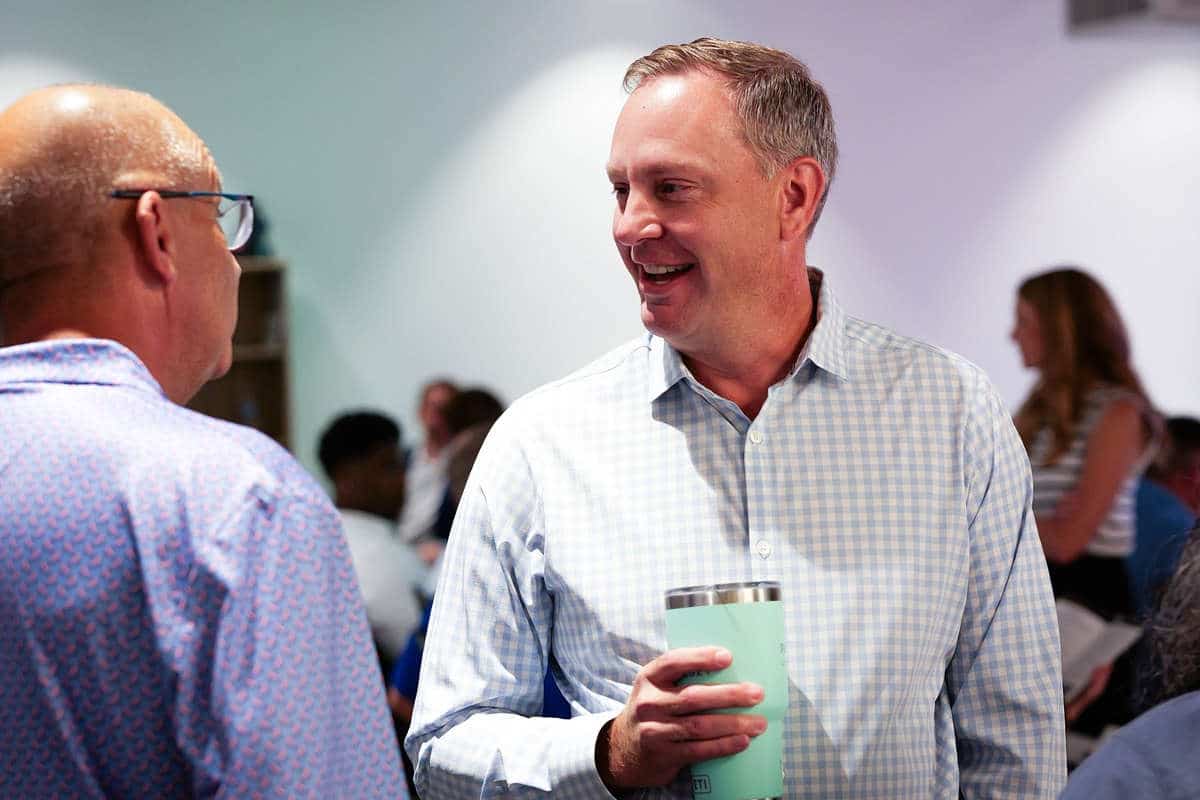 Mark Witkowski, holding a tumbler, in conversation with another attendee