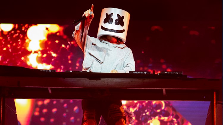 Marshmello performing in his white helmet behind a DJ console