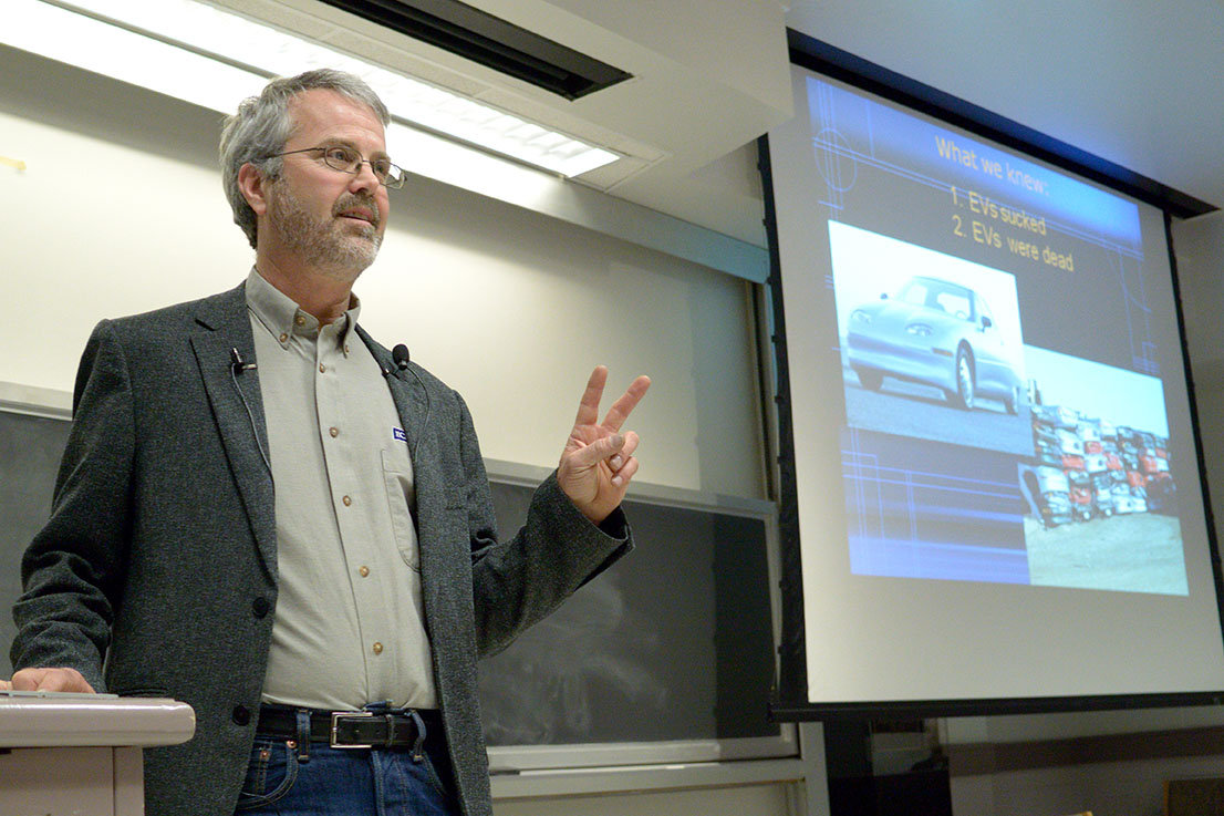 Martin Eberhard speaking at an Illinois engineering lecture in 2014, beside a projected slide about electric cars