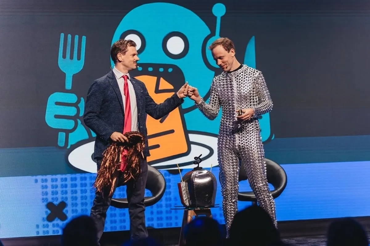 Martin Rand and a fellow Pactum founder exchange a fist bump on stage, beside a robot illustration.